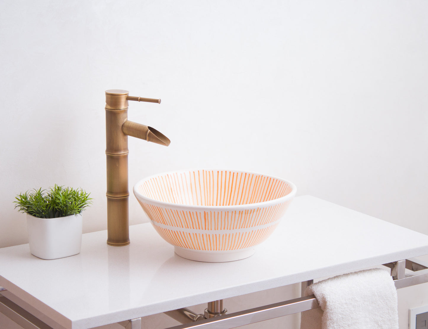 Round Moroccan ceramic basin installed on white bathroom vanity with bamboo-style brass faucet and decorative plant