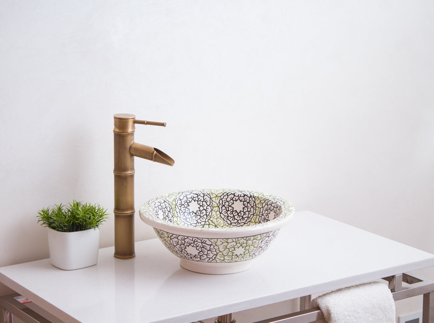 Moroccan ceramic wash basin styled on white vanity with brass bamboo faucet and decorative plant