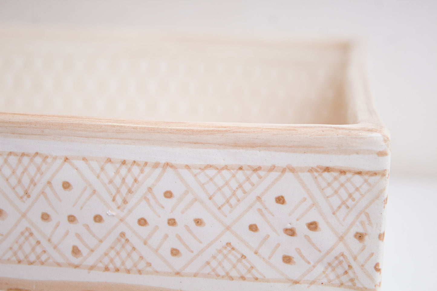 Close-up detail of intricate diamond and dot patterns on beige ceramic basin exterior rim