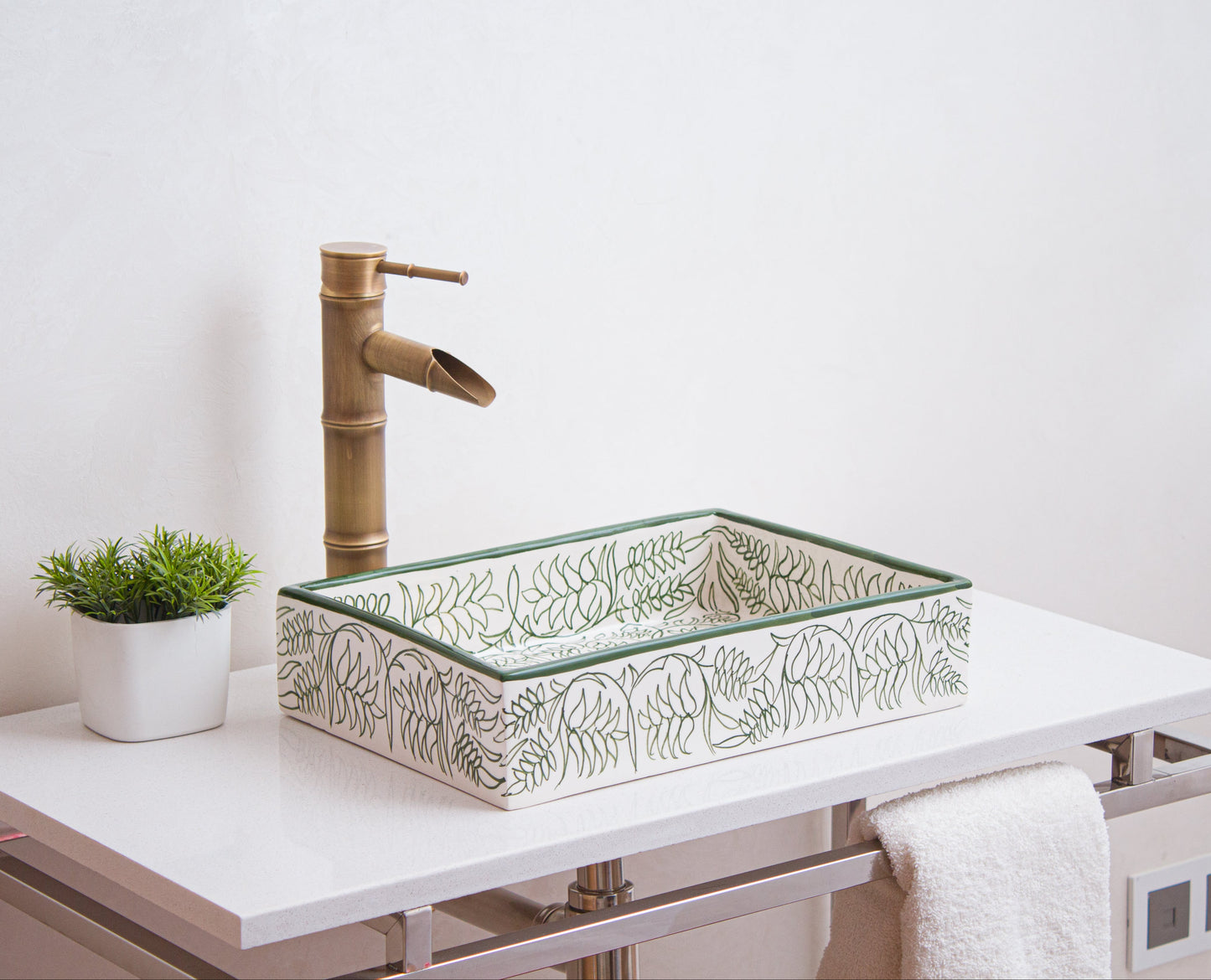 Handcrafted Moroccan ceramic rectangular sink with green botanical motifs displayed on white vanity with bamboo faucet and decorative plant