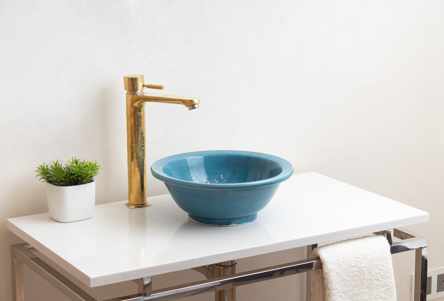 Blue ceramic vessel sink installed on white floating vanity with brass faucet, green plant, and white towel in contemporary bathroom