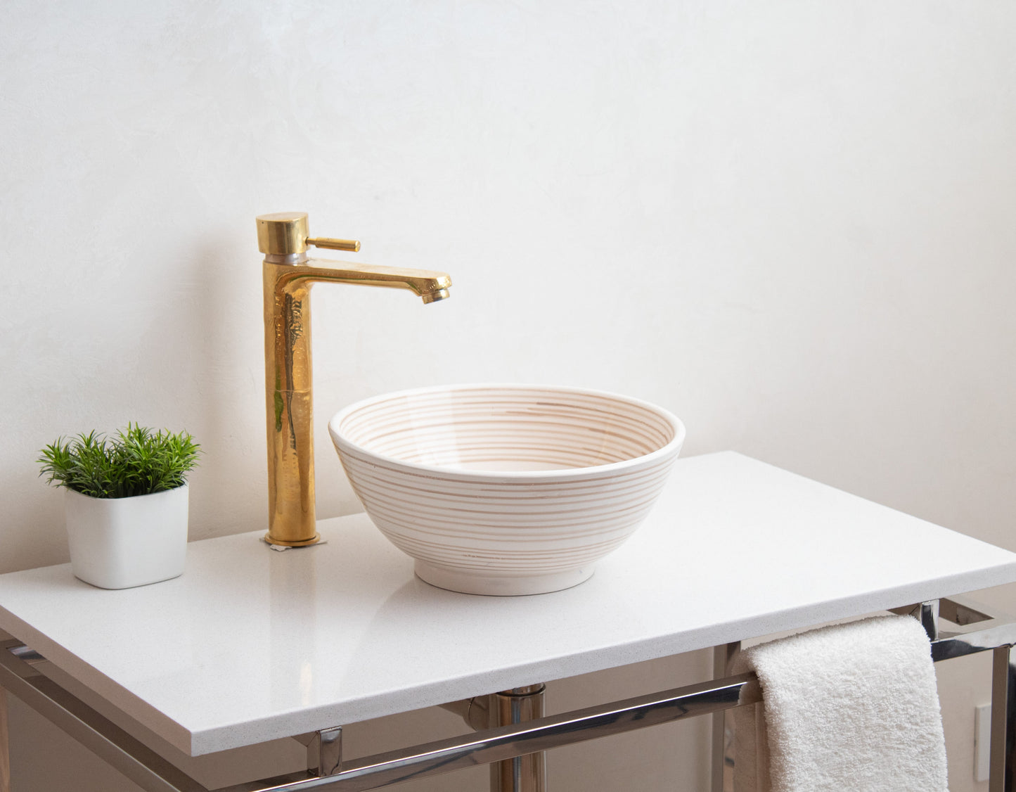 Cream ceramic vessel sink with spiral texture installed on white floating vanity with brass faucet and white towel in contemporary bathroom