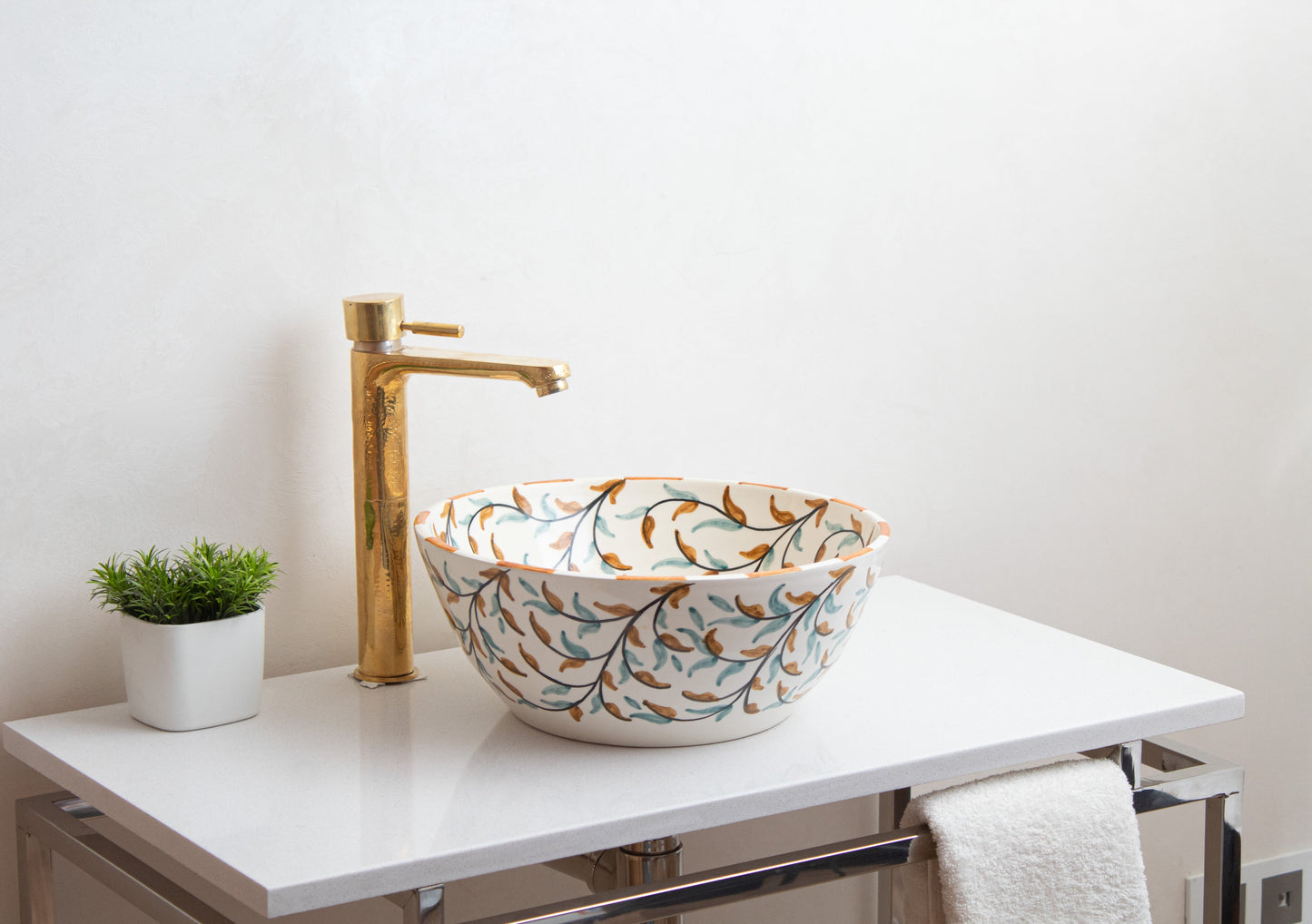 Ceramic vessel sink with painted olive motif installed on white floating vanity with brass faucet and white towel in contemporary bathroom