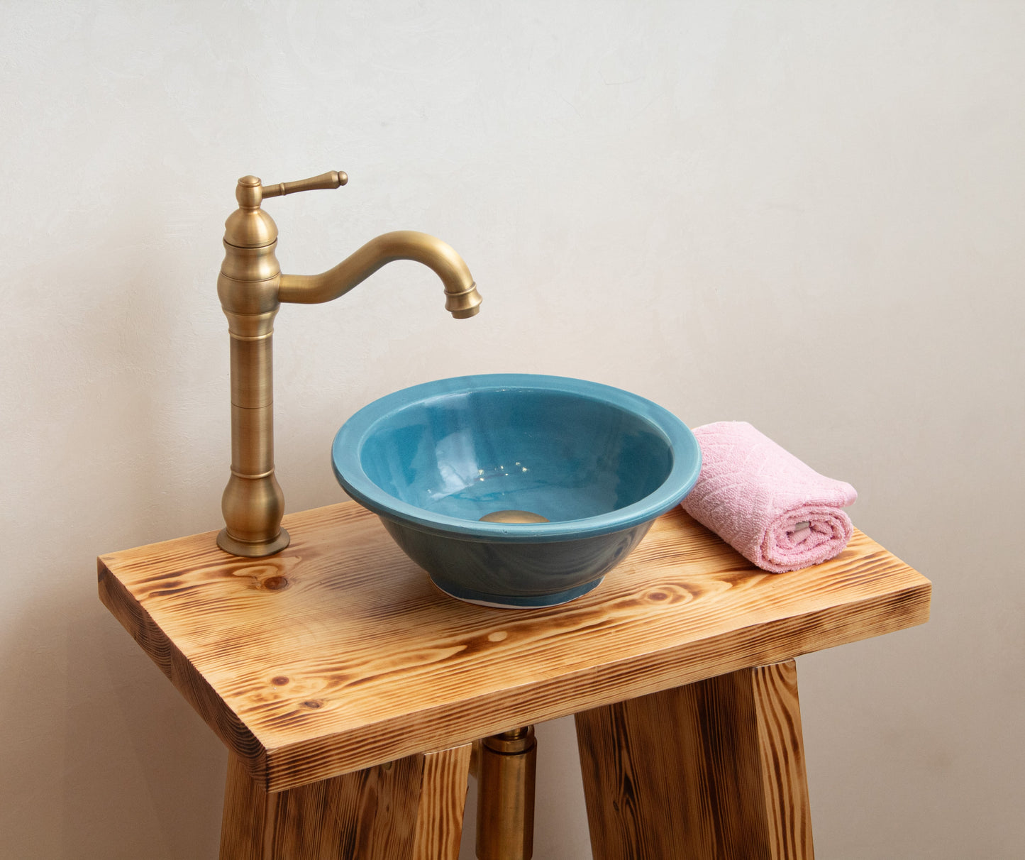 Blue ceramic vessel sink styled on rustic wooden vanity with brass faucet and pink towel in modern bathroom setting