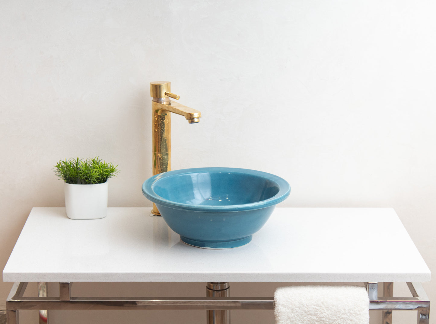 Blue ceramic vessel sink on white contemporary vanity with tall brass faucet and decorative green plant in minimalist bathroom