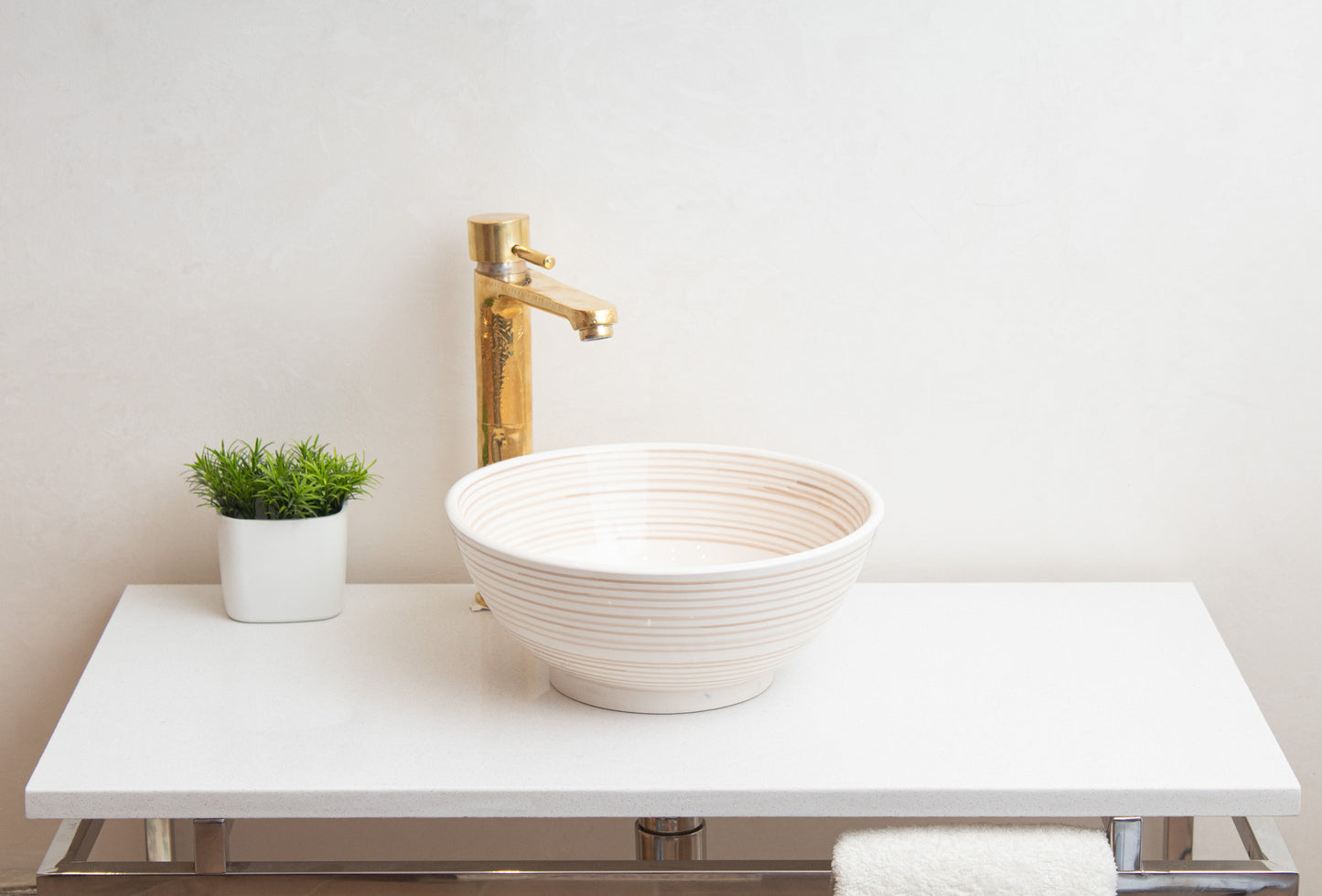Cream ceramic vessel sink with spiral texture on white contemporary vanity with tall brass faucet and decorative green plant