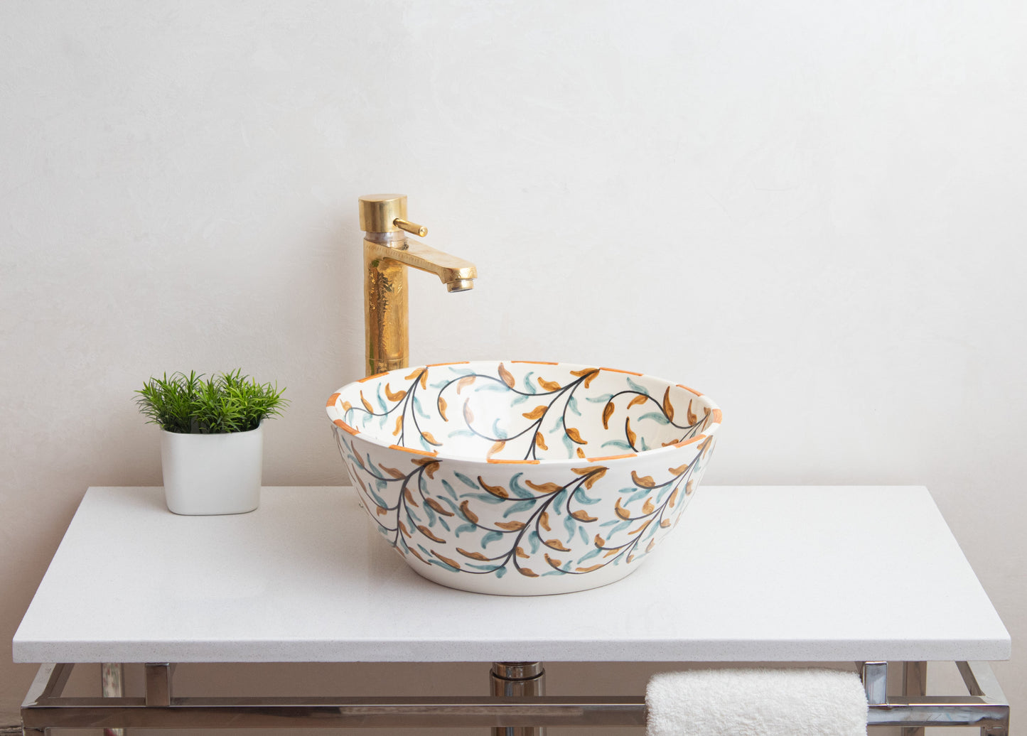 Ceramic vessel sink with olive garden pattern on white contemporary vanity with tall brass faucet and decorative green plant