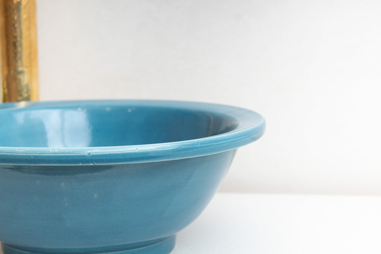 Close-up detail of blue ceramic vessel sink rim and curved bowl edge highlighting the glossy turquoise glaze finish