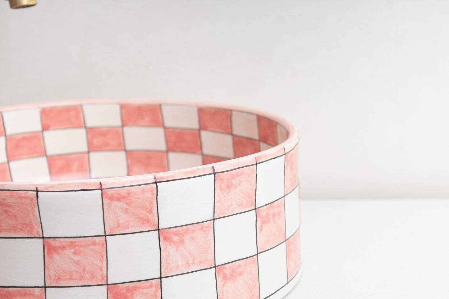 Close-up detail of ceramic vessel sink rim highlighting the pink and white checkered tile pattern and glossy finish