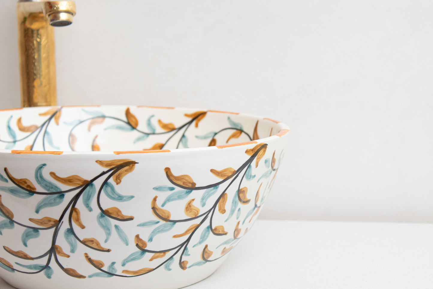 Close-up detail of ceramic vessel sink rim highlighting the hand-painted olive branch motif and orange accent border