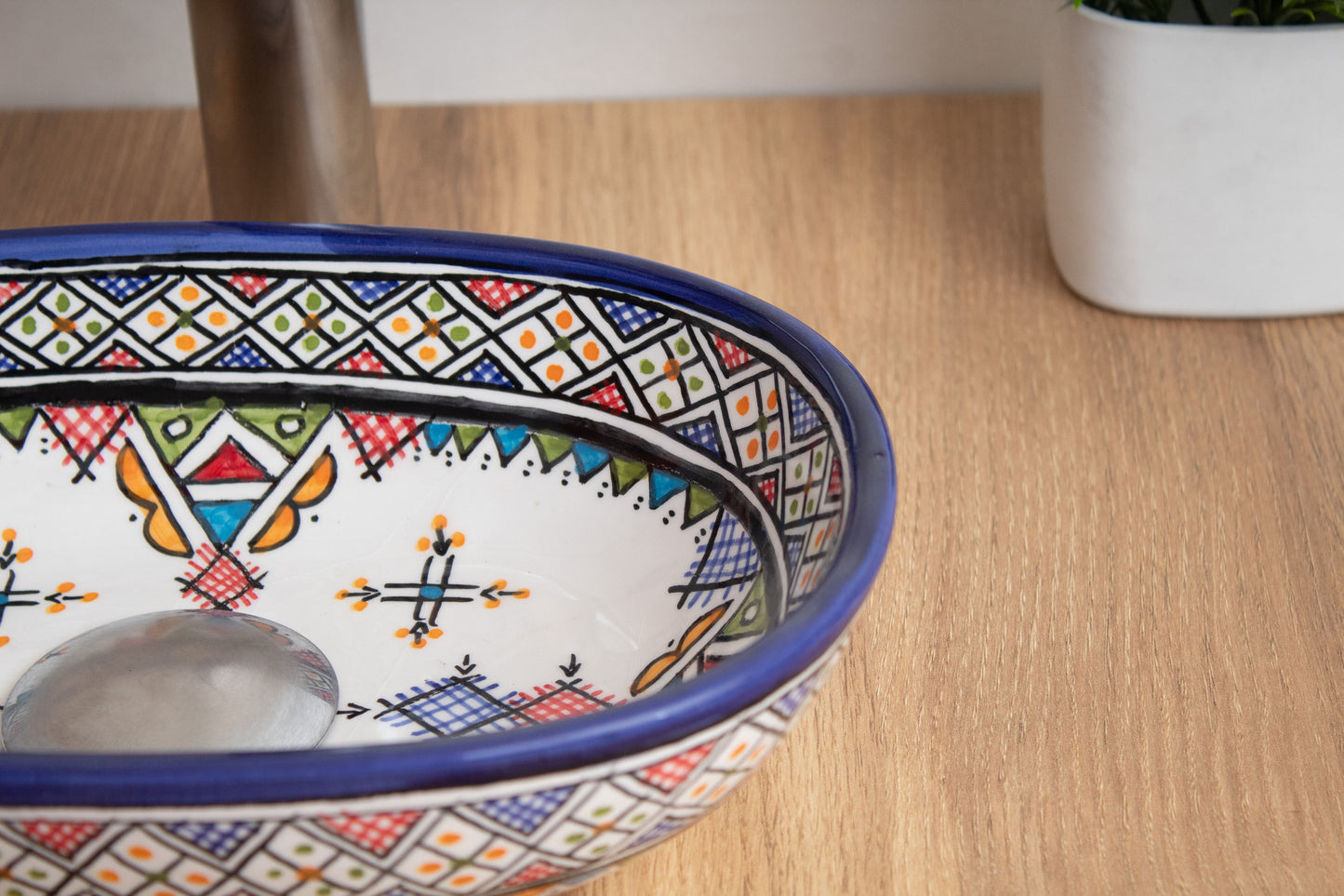 Close-up interior detail of compact oval ceramic vessel sink showing traditional Amazigh cross and star motifs with drain opening on wood surface