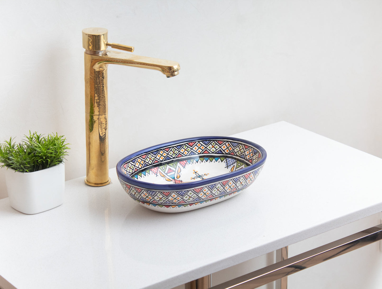 Small oval ceramic vessel sink with traditional Amazigh geometric patterns on white contemporary vanity with tall brass faucet and decorative green plant
