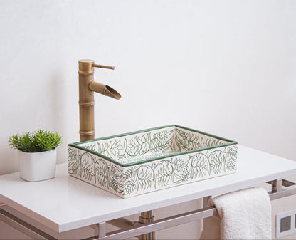 Handcrafted Moroccan ceramic rectangular sink with green botanical motifs displayed on white vanity with bamboo faucet and decorative plant