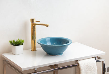 Blue ceramic vessel sink installed on white floating vanity with brass faucet, green plant, and white towel in contemporary bathroom