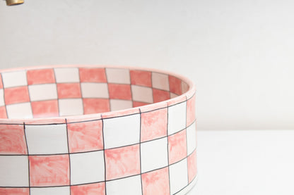 Close-up detail of ceramic vessel sink rim highlighting the pink and white checkered tile pattern and glossy finish